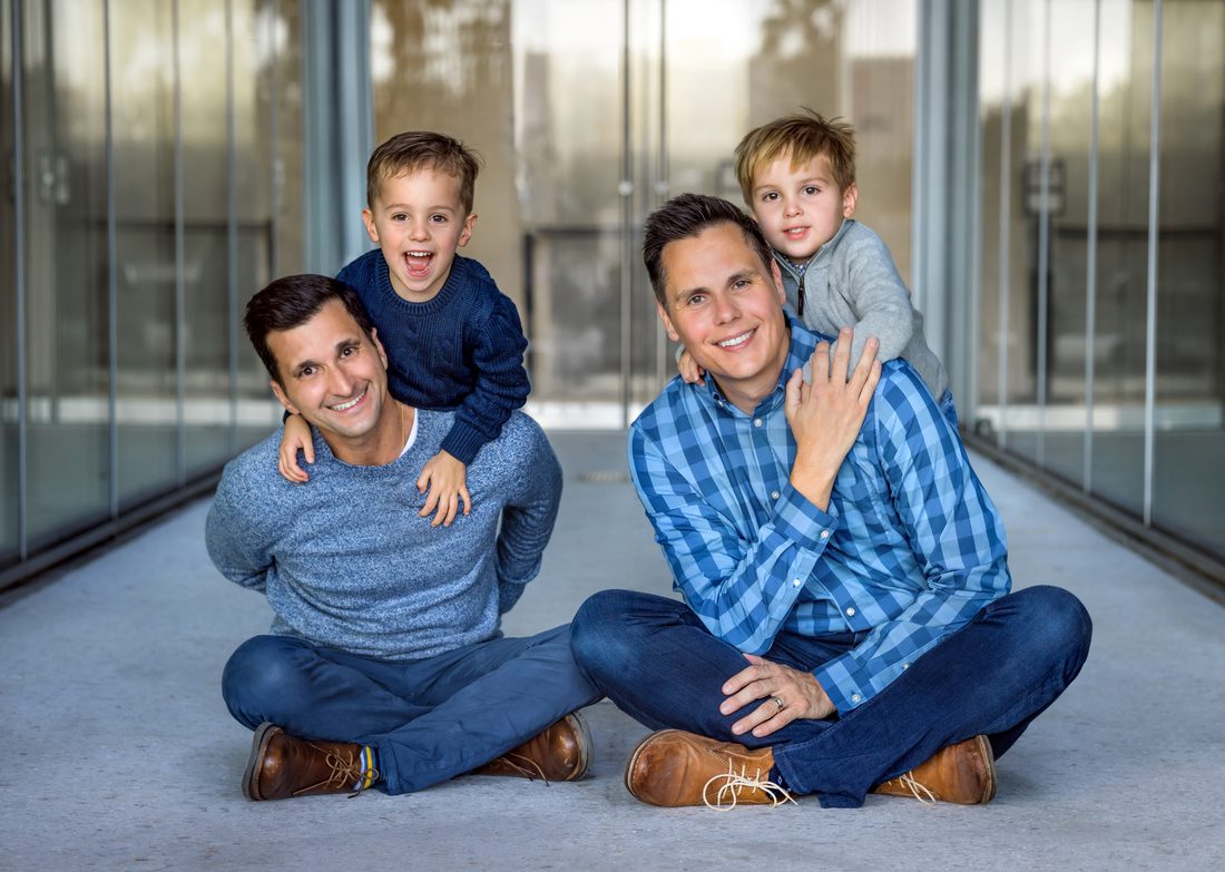 Two dads sitting with their two sons in a modern hallway