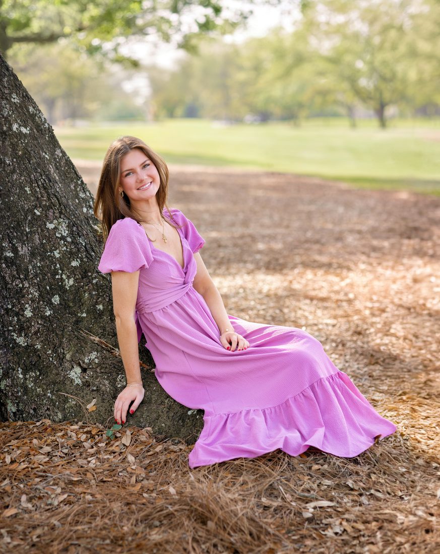 Senior portrait seated against an oak tree