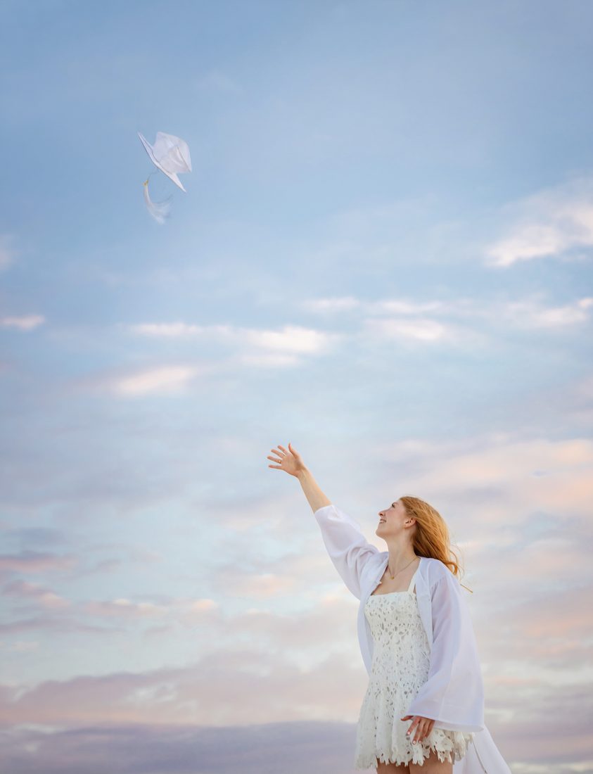 Senior portrait tossing fabric into a sunset sky
